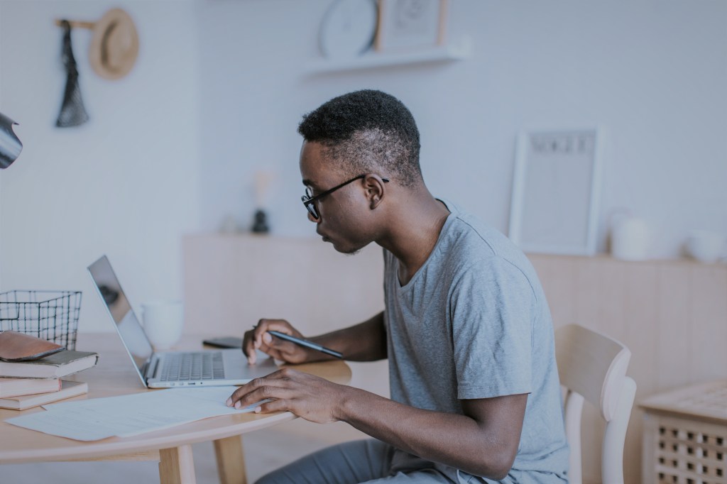 Homem em um escritório, mexendo no notebook e fazendo anotações aprendendo sobre como investir em fundos imobiliários com a Clear Corretora. 