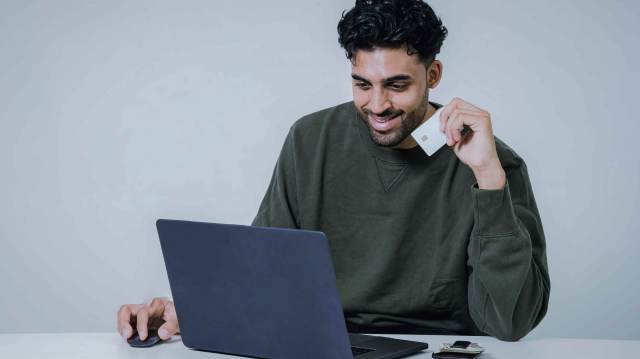 A foto mostra um homem sorrindo, vestindo um moletom verde. Ele está usando um notebook, em referência a operação do RLP.