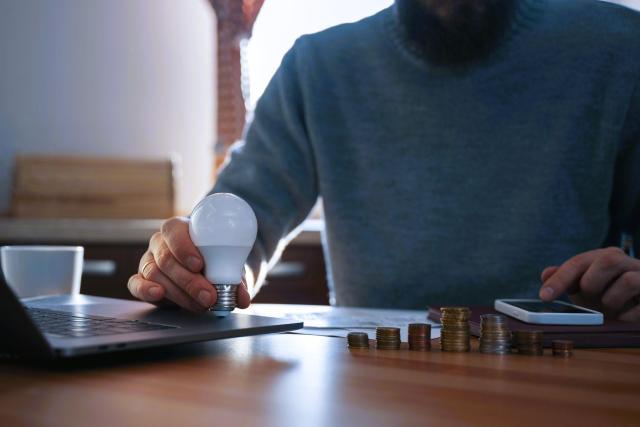 Investidor segurando uma lâmpada sobre seu laptop, simbolizando a clareza ao descobrir seu tipo de perfil de investidor e organizar suas finanças, com pilhas de moedas ao lado.