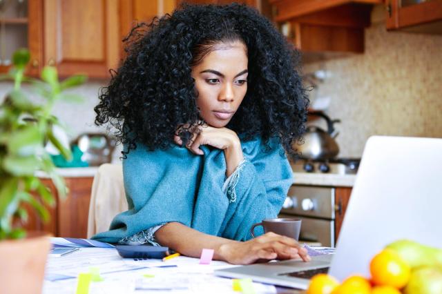 Investidora com expressão concentrada, apoiando o queixo na mão enquanto analisa informações sobre seu perfil de investidor em um laptop.