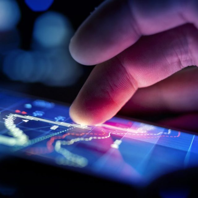 A foto mostra um dedo mexendo em um celular em uma plataforma de investimentos