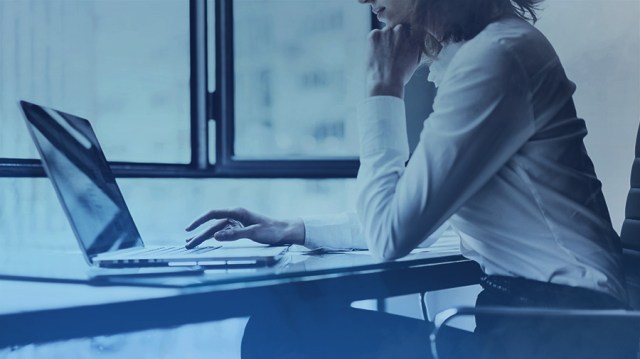 Uma moça com roupa social sentada no escritório mexendo em seu notebook, pesquisando sobre como investir na bolsa.