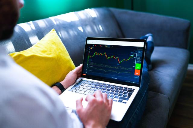 Pessoa sentada no sofá com um notebook no colo, acompanhando gráficos financeiros para começar a investir na bolsa.