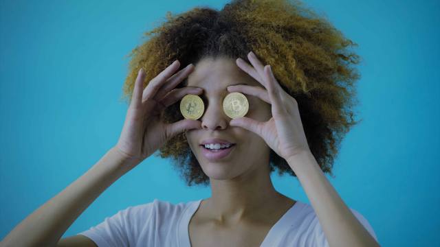 Na imagem temos uma mulher negra com seu cabelo afro, segurando duas moedas nos olhos.