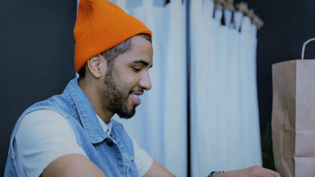 A imagem mostra um homem negro de barba vestindo uma touca laranja e uma camisa branca com um colete jeans por cima. Ele está sorrindo em referência as vantagens do mercado futuro.