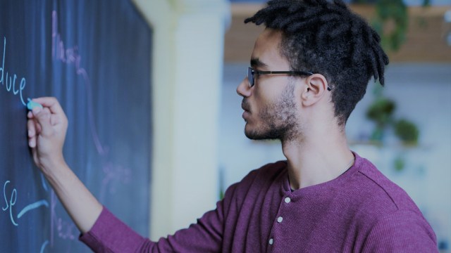 Homem negro de óculos escrevendo em uma lousa, representando a explicação dos códigos de opções e a importância de entender a nomenclatura para investir com segurança.