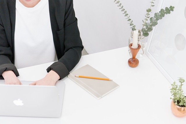 mulher mexendo em notebook da Apple, com um caderno fechado ao lado