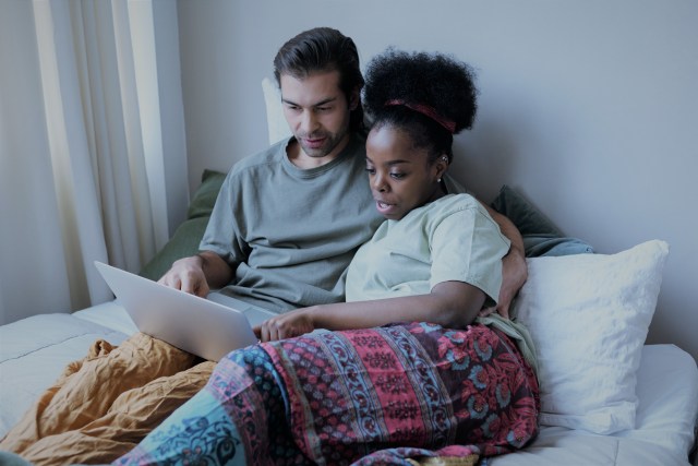 Casal deitado na cama em frente ao computador lendo sobre as ações da magazine luiza