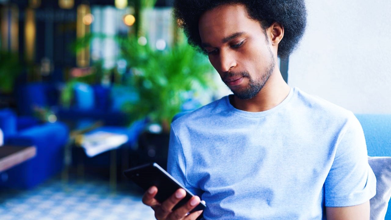 Homem em ambiente interno pesquisando em seu celular como abrir conta na Clear para investir em HASH11.