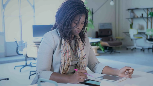 Mulher negra em frente à uma mesa com um tablet e uma caneta na mão direita, aprendendo sobre os diferentes tipos de ações (ON, PN, Units) para começar seus investimentos.