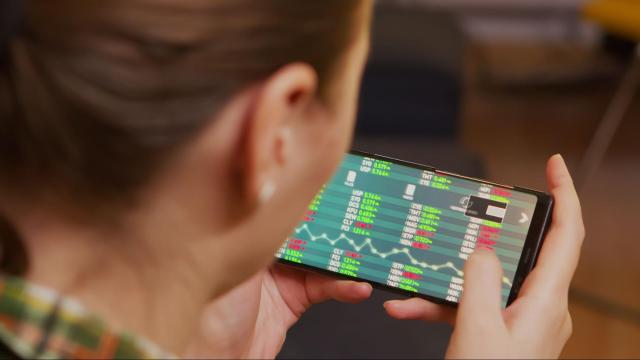 Mulher branca analisando tipos de ações em um smartphone, representando a importância de estar informado para começar os investimentos.