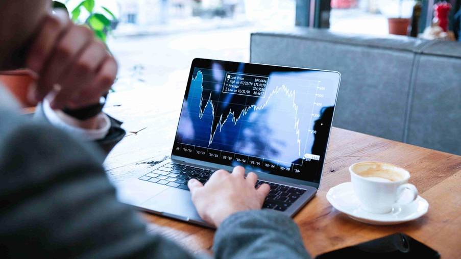 Pessoa analisando gráfico de ações em notebook, ilustrando conceitos da teoria de Dow, como tendências de mercado.