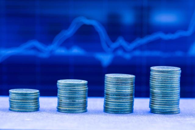 Pilhas de moedas em ordem crescente com um gráfico de ações subindo ao fundo, representando o ibovespa em máxima histórica.