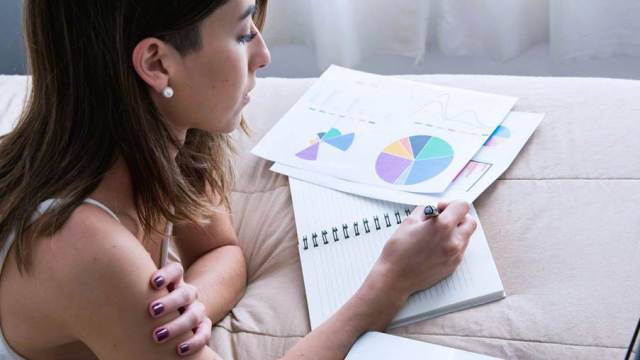 Mulher fazendo anotações em um caderno sobre o ponto de equilíbrio da empresa, a partir da análise de gráficos impressos.