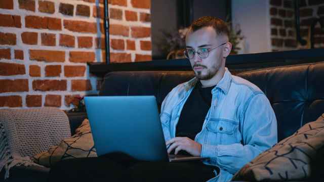 Homem sentado em um sofá com o notebook apoiado sobre as pernas, pesquisando como investir em ações da Vale.