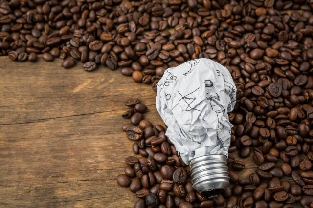 Lâmpada de papel amassado simbolizando ideias e estratégias para investir em contrato futuro de café, sobre uma superfície com grãos de café torrados.