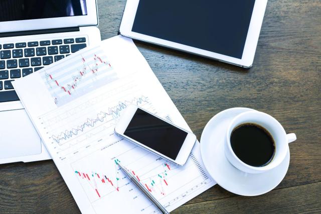 Mesa de trabalho com gráficos de análise da cotação do café para operar contrato futuro, ao lado de um notebook e uma xícara de café.