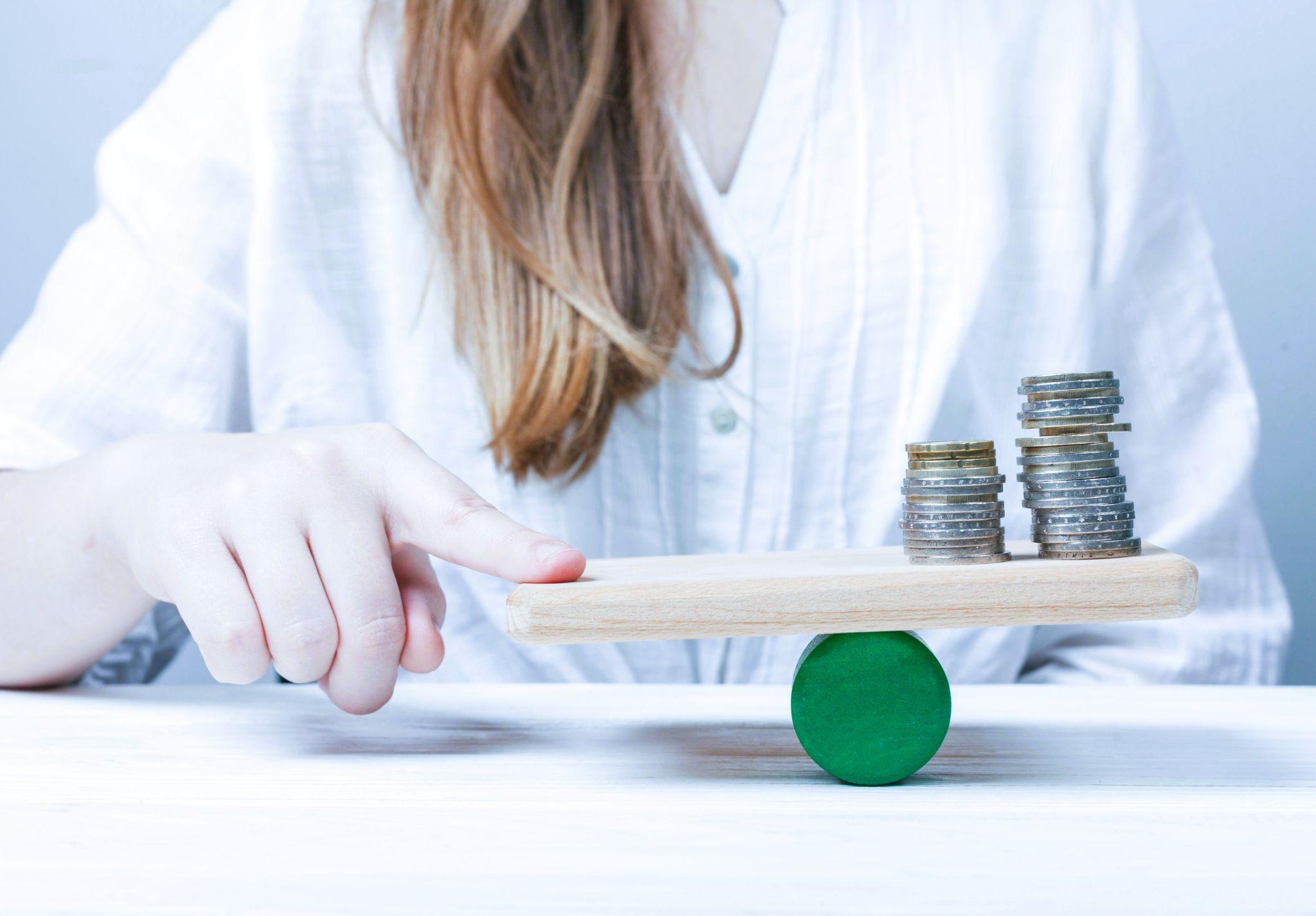 Mulher equilibrando moedas em uma balança pequena, representando a restituição do IR no day trade.