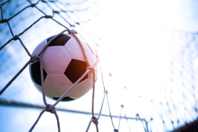 Close de uma bola de futebol atingindo o fundo da rede um gol, representando a oportunidade de “golear” com as melhores ações para investir na copa.