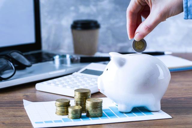 Mão depositando uma moeda em um cofrinho, com calculadora e computador ao fundo, representando o planejamento para quem busca entender o que é renda fixa
